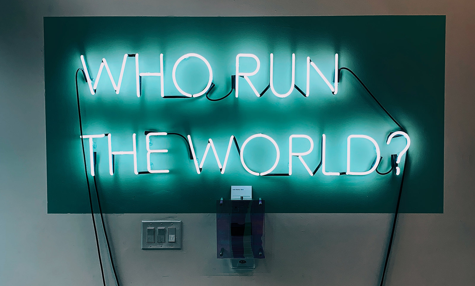 A neon sign reads who run the world?