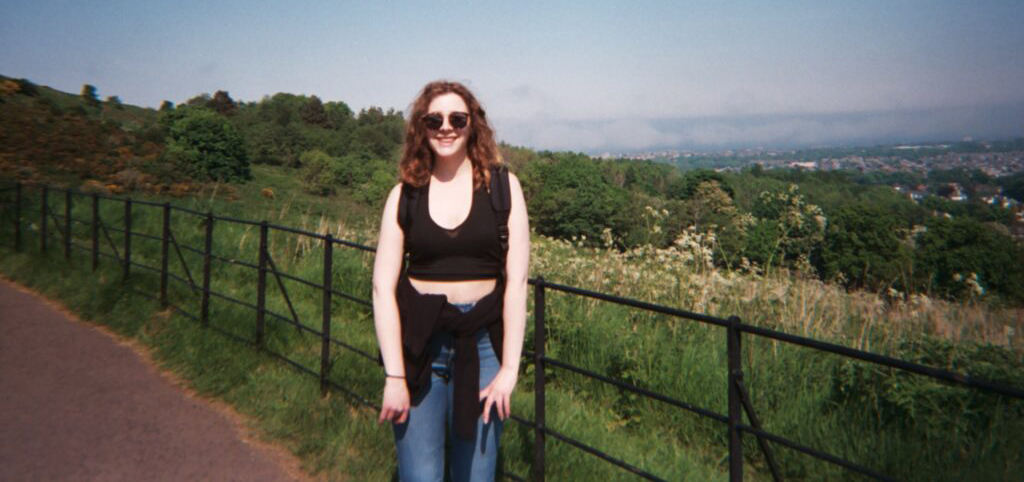 Student posing for the camera on a sunny day with a green landscape behind.
