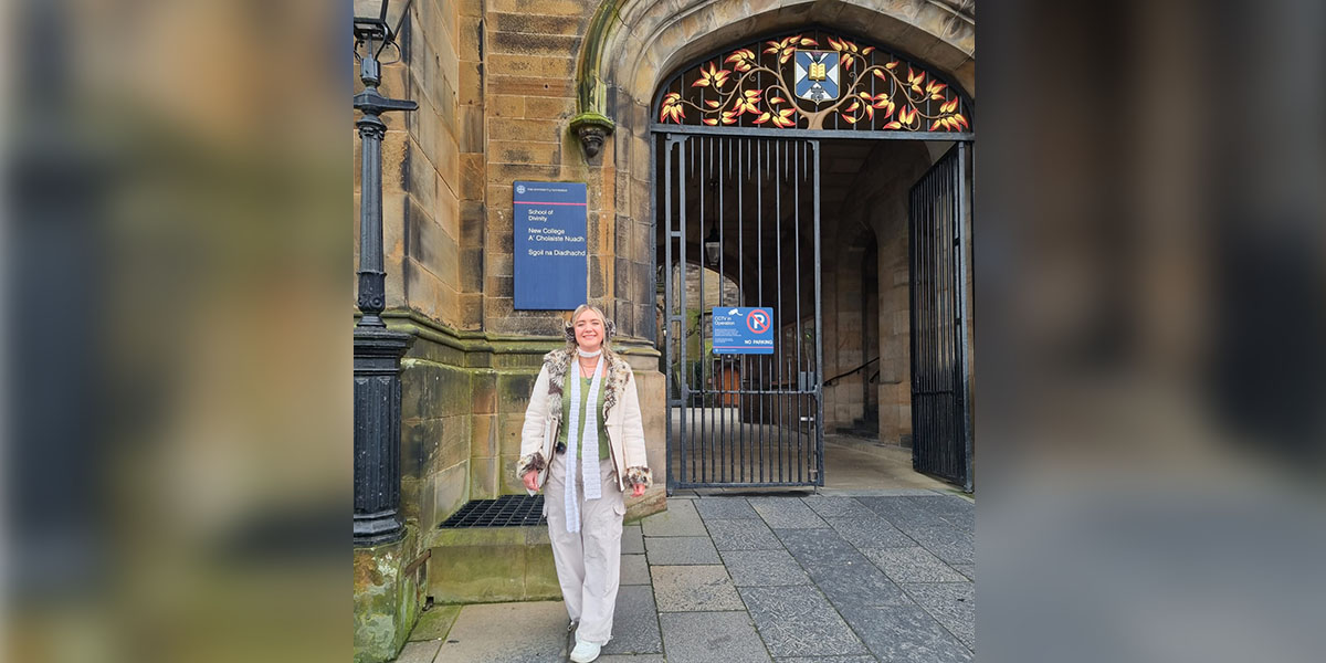 Maisie stands in front of an arched entrance to the School of Divinity,