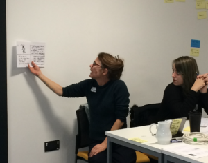 Woman hold paper containing sketch aloft while speaking