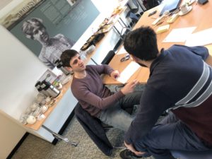 Two students discuss, seated at desk